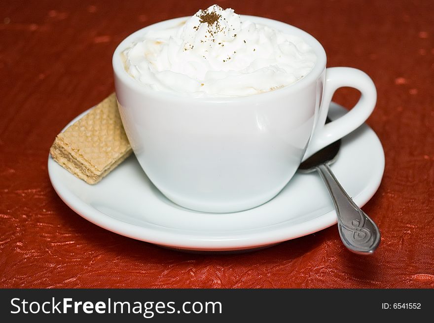 Cup of cappuccino strewed by grated chocolate on deep red background