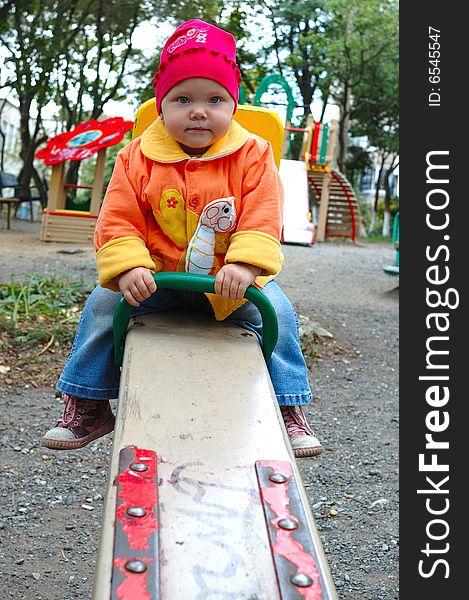 Pretty little girl with bright jacket sit on seesaw (teeter-totter). Pretty little girl with bright jacket sit on seesaw (teeter-totter).