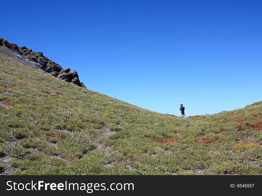 A lone hiker in a steep mountain saddle in the Sierra Nevada mountains.  California, U.S.A. A lone hiker in a steep mountain saddle in the Sierra Nevada mountains.  California, U.S.A