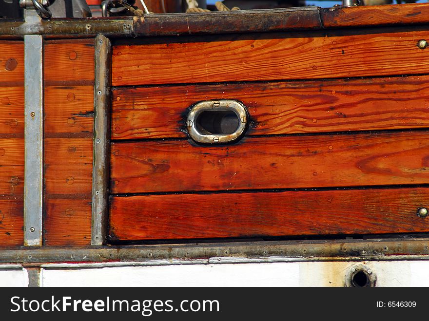 Detail of wooden planks and copper porthole on traditional wood schooner. Detail of wooden planks and copper porthole on traditional wood schooner.