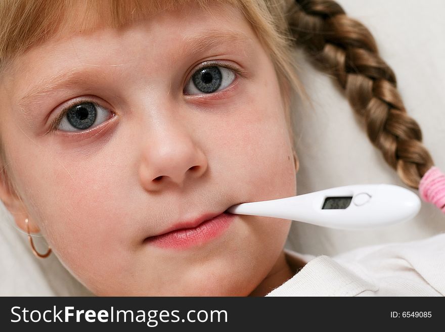Child in bed under blanket with thermometer in mouth