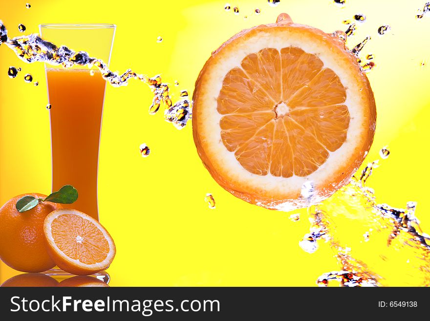 View of piece of orange getting splashed  and  glass of juice on back