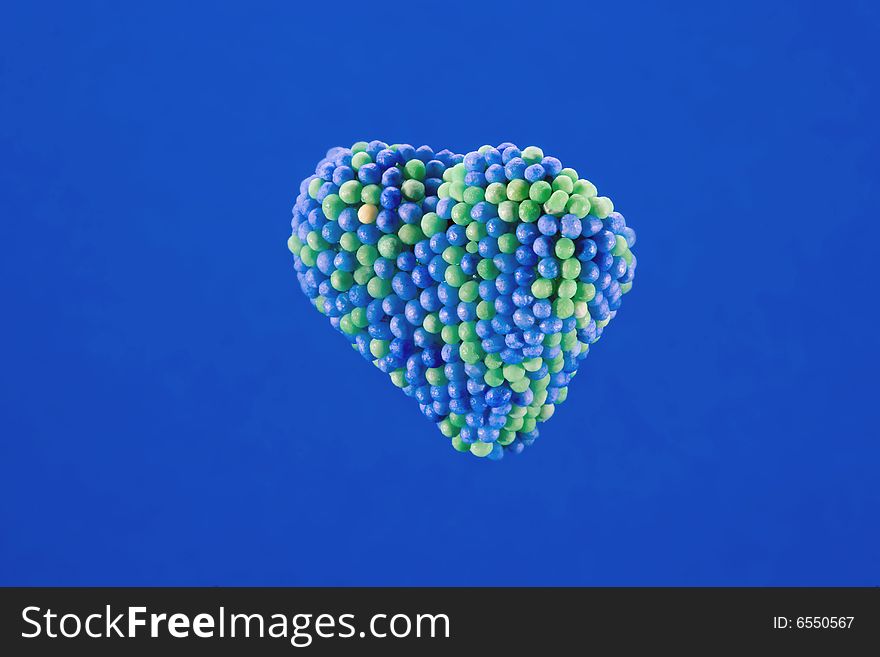 Candy heart encrusted with blue and green colored sugar balls, isolated on blue background