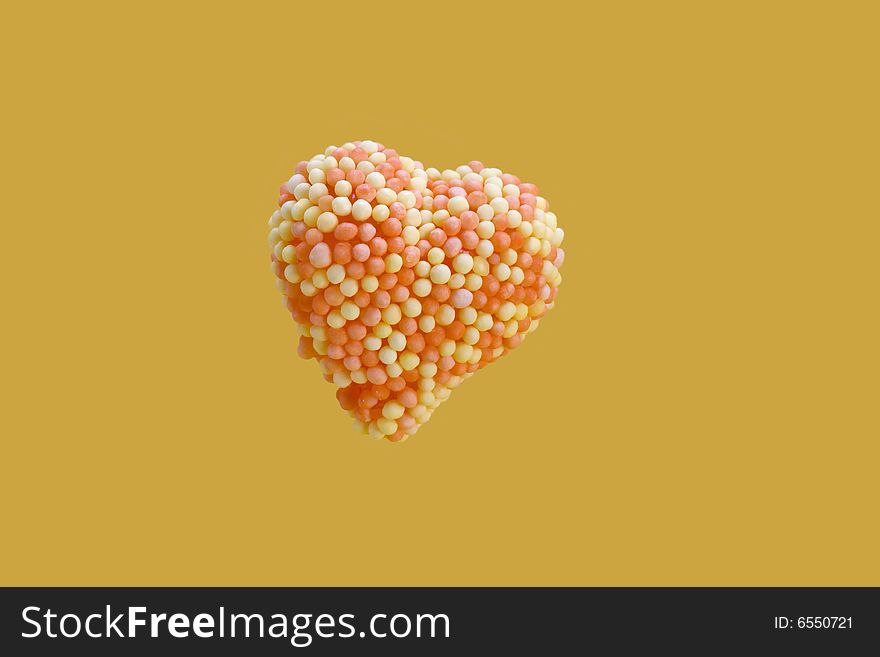 Candy heart encrusted with yellow and orange colored sugar, balls isolated on yellow background