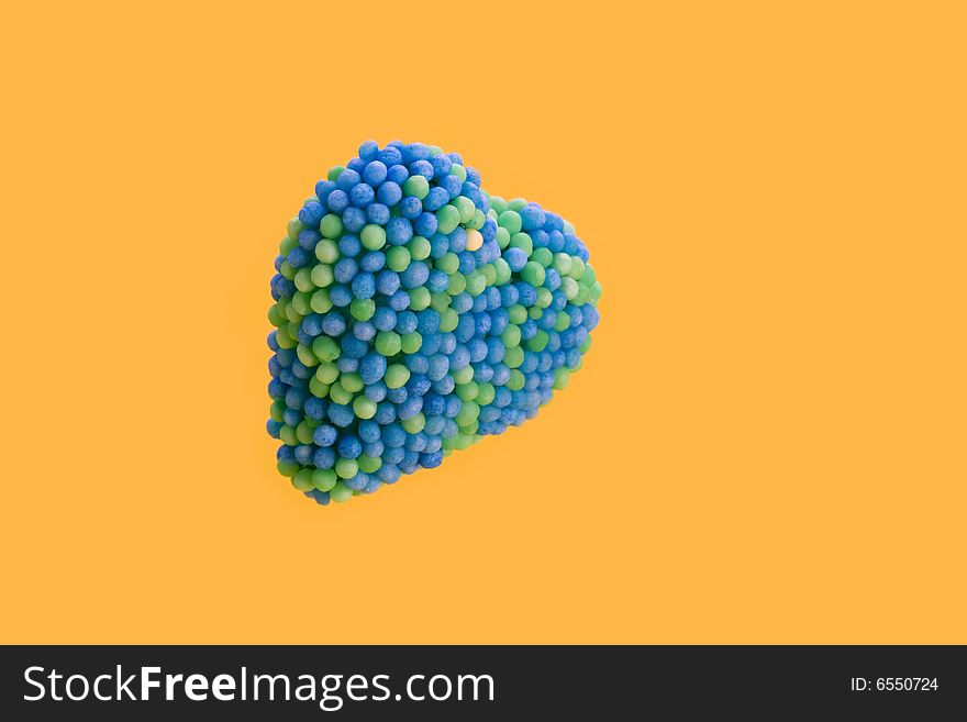 Candy heart encrusted with blue and green colored sugar balls isolated on yellow background