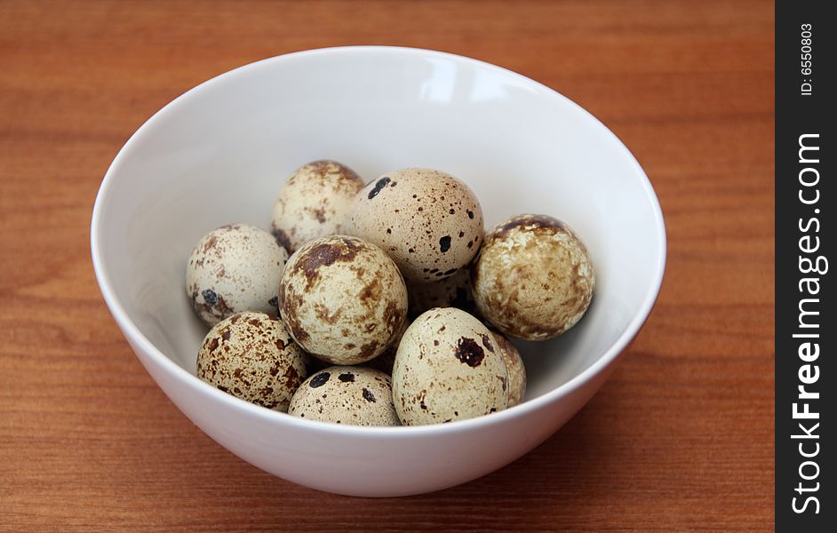 Quail eggs in a bowl on a wooden surface