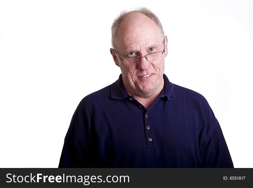 An older bald guy in a blue shirt smiling over his glasses. An older bald guy in a blue shirt smiling over his glasses