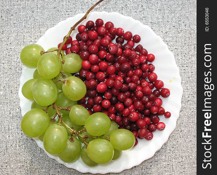 The autumn still life. Green grape, cranberries and helenium on the white  plate.