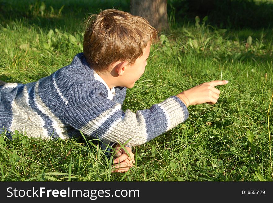 The boy lies on a grass and points a finger