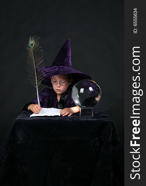 Wizard child next to crystal ball writing a spell with a peacock feather pen. Wizard child next to crystal ball writing a spell with a peacock feather pen