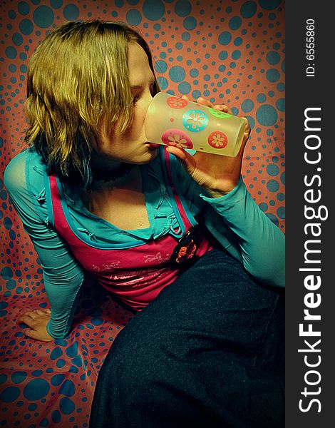 Stylish girl is sitting and drinking from plastic glass. Primary colors are pink and blue. Stylish girl is sitting and drinking from plastic glass. Primary colors are pink and blue.