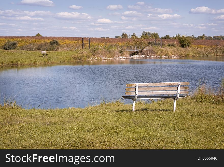 Wooden bench overlooking blue lake in early autumn day. Wooden bench overlooking blue lake in early autumn day