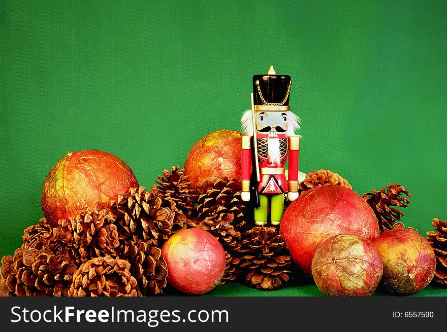 Nutcracker with pnecones and red ball ornaments on rustic green background. Nutcracker with pnecones and red ball ornaments on rustic green background