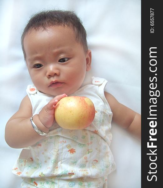 Pretty baby and red apple on a bed