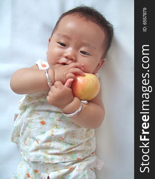 Pretty baby and red apple on a bed