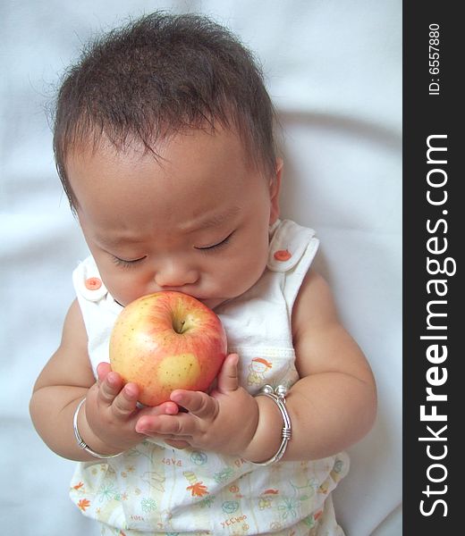 Pretty baby and red apple on a bed