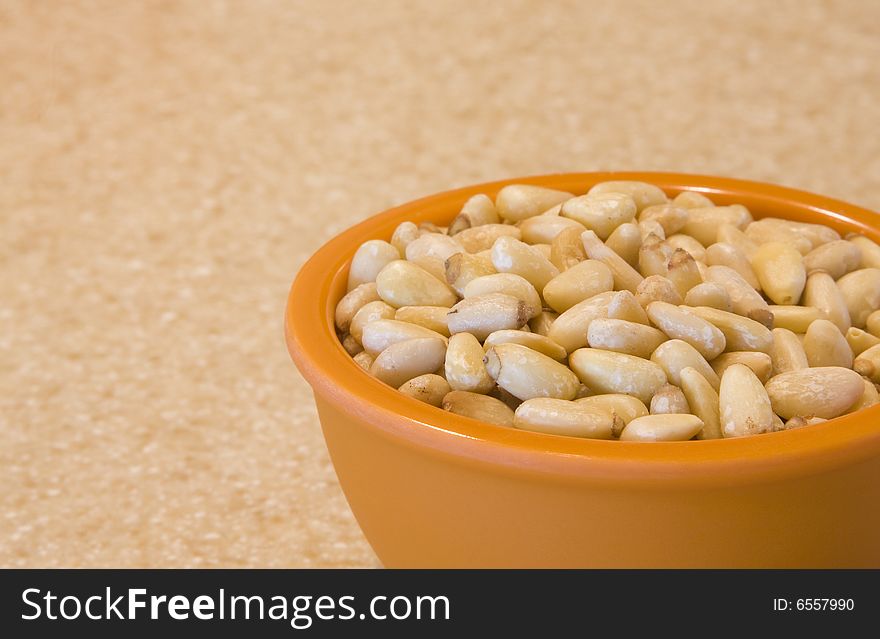 Pine nuts in an orange bowl on a counter. Pine nuts in an orange bowl on a counter.