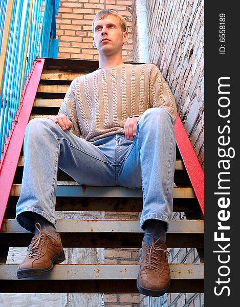 Young stylish man with blonde hair sit on stairs near brick wall. Young stylish man with blonde hair sit on stairs near brick wall.