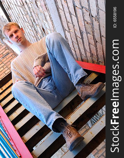 Young stylish man sit on stairs near brick wall.