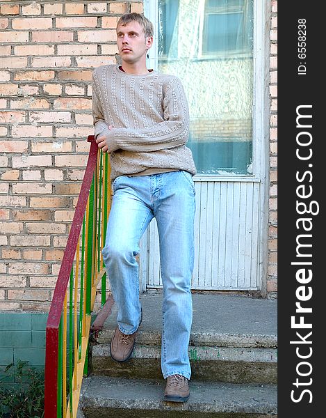 Young stylish man with blonde hair stay on stairs near brick wall. Young stylish man with blonde hair stay on stairs near brick wall.