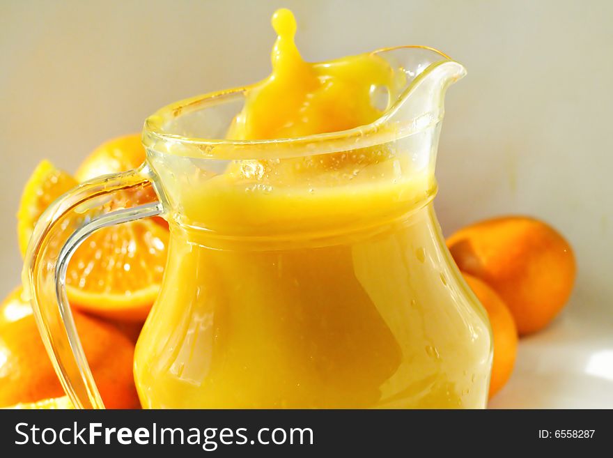 A glass of orange juice with oranges around it and a refrshing splash