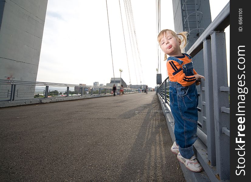 Little girl show tongue hold to fence on bridge