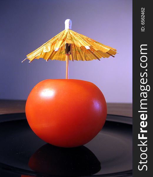Red tomato with party umbrella on a blue background. Red tomato with party umbrella on a blue background.