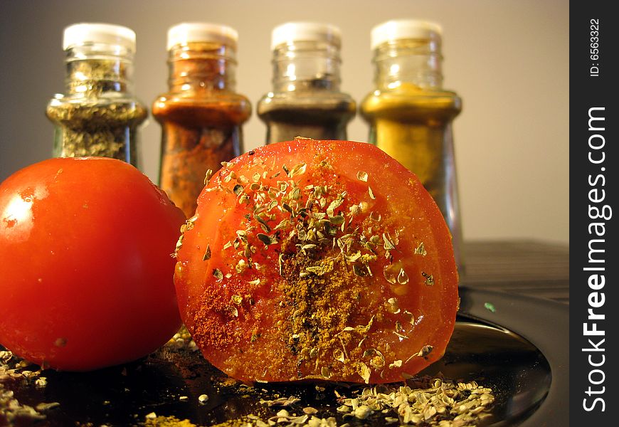 Ripe tomato cut on half with pepper, oregano, curry and red paprika on it and standing behind. Ripe tomato cut on half with pepper, oregano, curry and red paprika on it and standing behind.