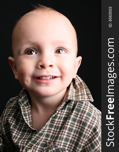 Blonde toddler against a black background with a big smile