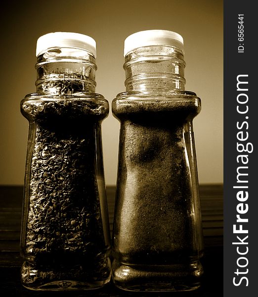 Oregano and pepper standing in glass jars in brown color.