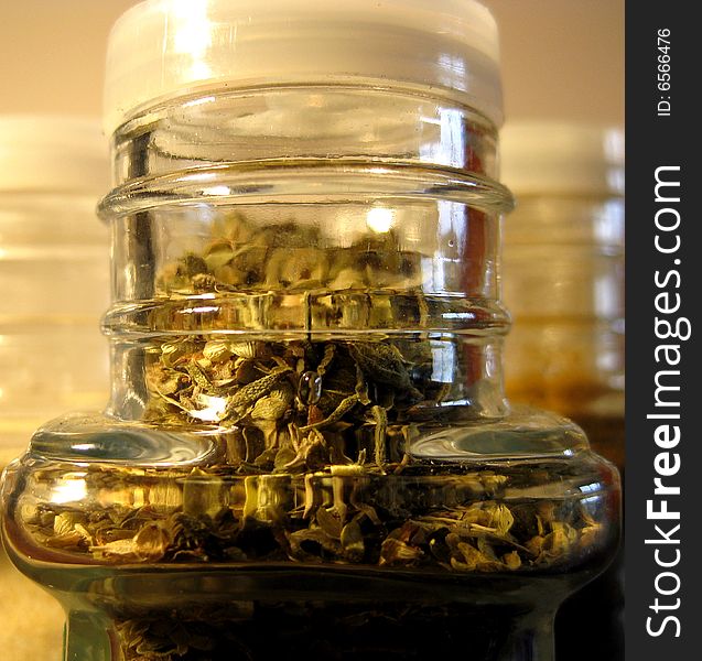 Oregano closeup of plastic top of glass jar and other spices standing behind.