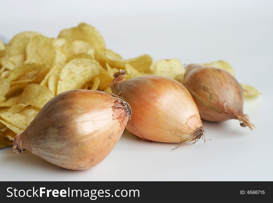 Close-up of three yellow onions and potatoe chips on background
