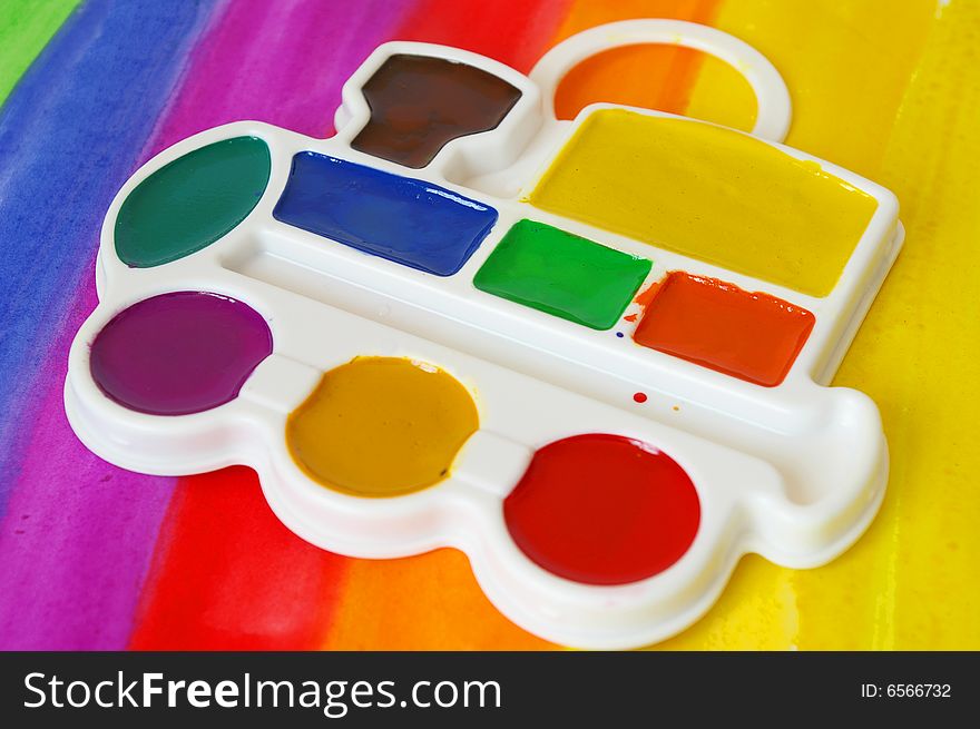 Box of watercolors and a brush on a colorful  background.