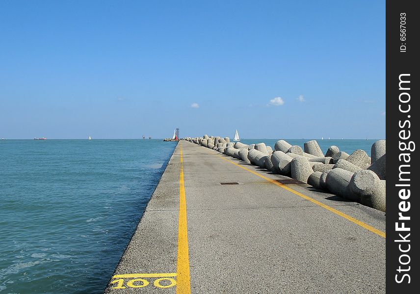 Long pier with parallel yellow lines going to the horizon surrounded by blue sky and blue sea