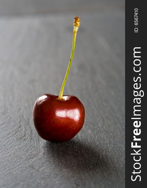 Single red cherry on a slate background