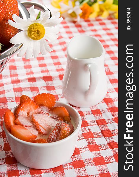 Sliced strawberries and cream in a white pot with a daisy on a red and white cloth