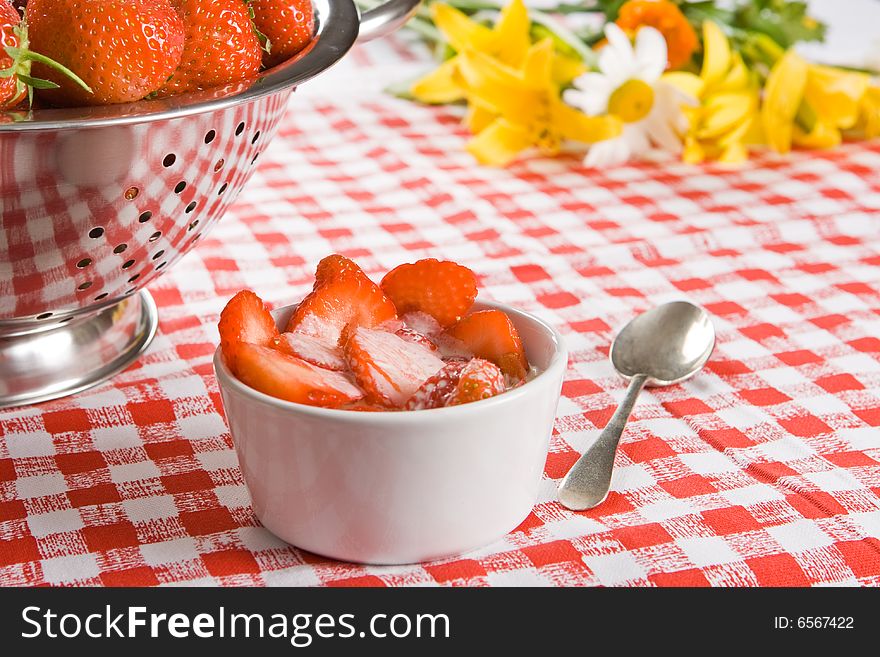 Sliced strawberries and cream in a white pot with flowers in the background