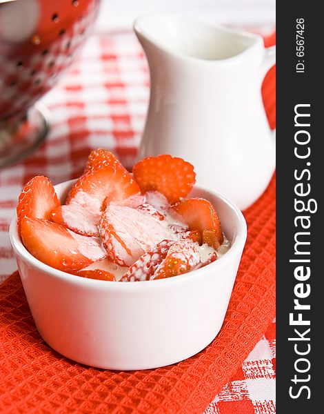 Fresh sliced strawberries with cream in a white pot on a red cloth