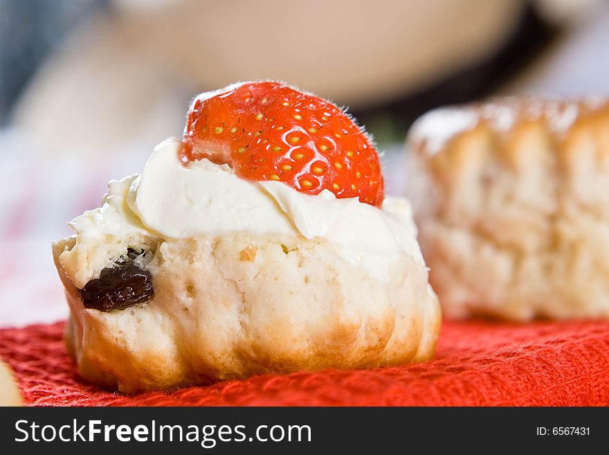 Close up of a scone with clotted cream and a strawberry on a red cloth