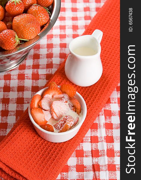 Sliced strawberries with cream in a white pot on a red cloth