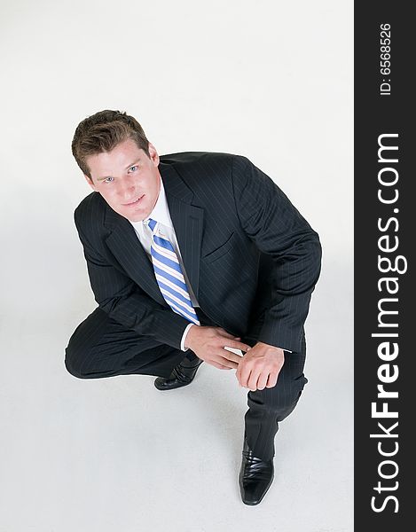 Young businessman squats down on grey background. Young businessman squats down on grey background