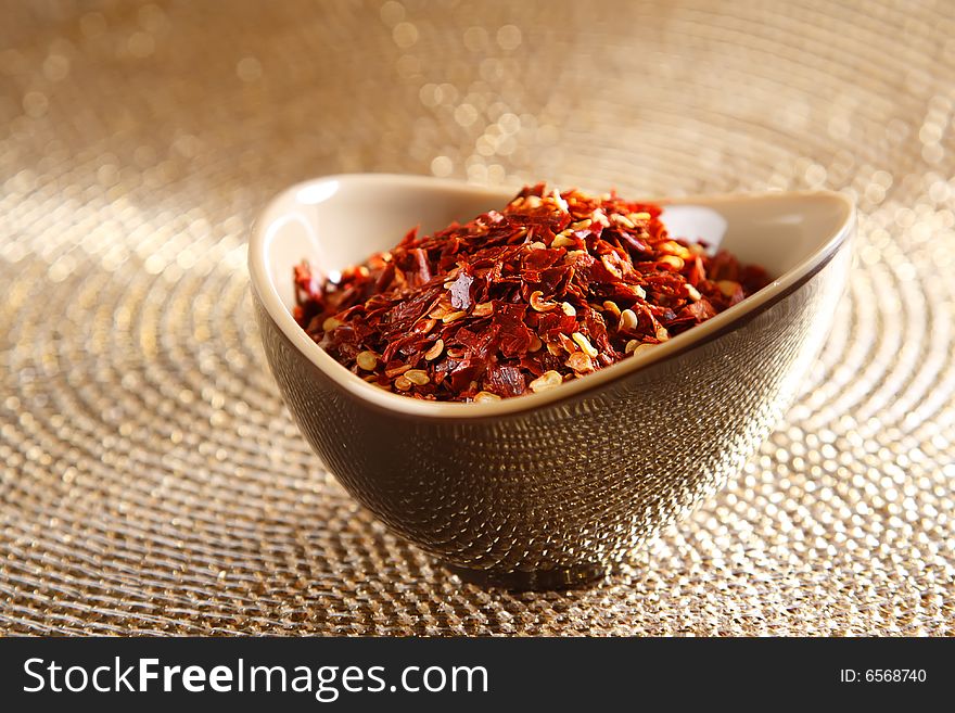 Crushed red hot chilli pepper in bowl on golden glitter background, shallow DOF