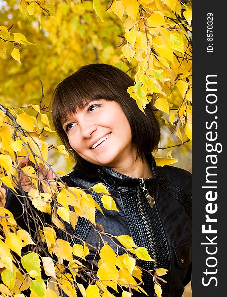 Cheerful cute girl in the park looking at yellow leaves