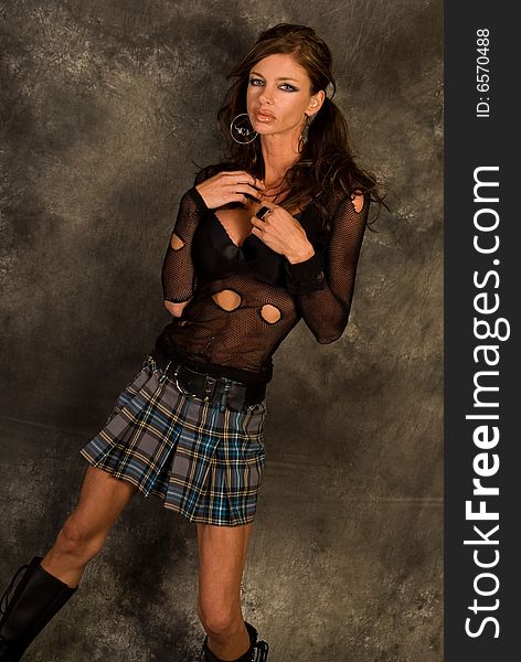 Brunette female fashion model in torn up black gothic see through top and plaid mini skirt against black and grey background in the studio. Brunette female fashion model in torn up black gothic see through top and plaid mini skirt against black and grey background in the studio