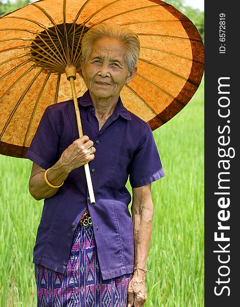 Old Asian woman with parasol on a rice-field in Thailand