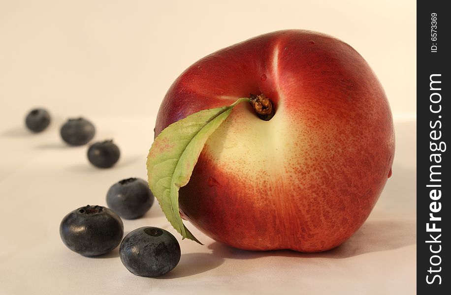 Peach and blueberries on eggshell white background. Focus on peach. Peach and blueberries on eggshell white background. Focus on peach.