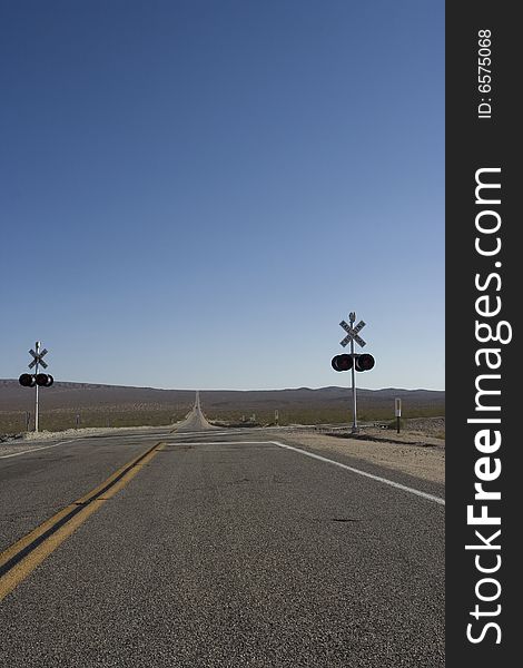 A point were a train can cross the road in death valley. In the back you see the endless road going on and on. A point were a train can cross the road in death valley. In the back you see the endless road going on and on.