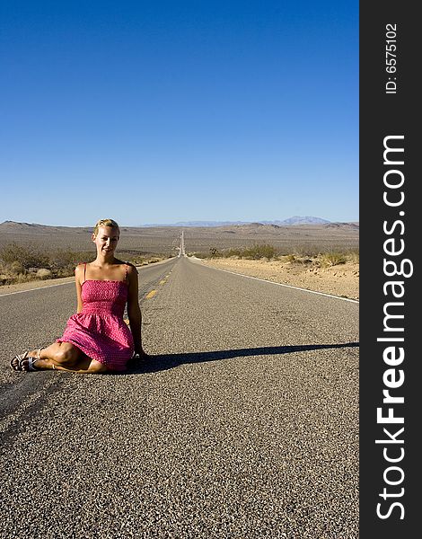 A woman in a pink dress that is sitting on a deserted road in death valley. A woman in a pink dress that is sitting on a deserted road in death valley.