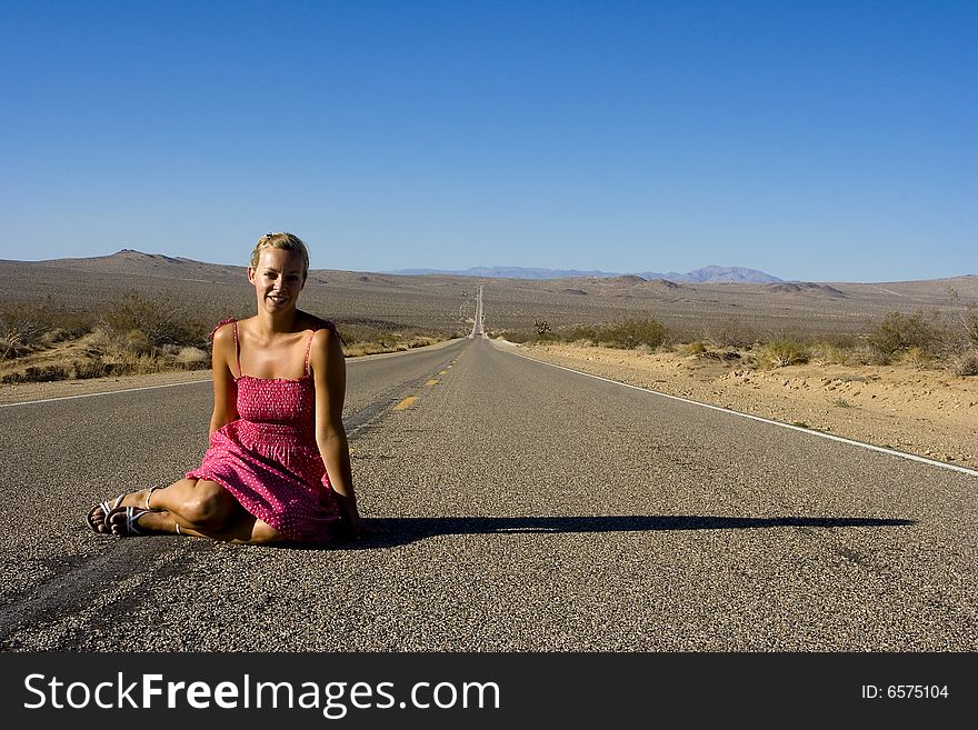 A woman in a pink dress that is sitting in the blazing heat on a deserted road in death valley. A woman in a pink dress that is sitting in the blazing heat on a deserted road in death valley.