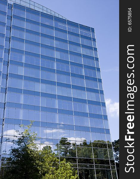 A blue glass office tower with clouds and trees reflected